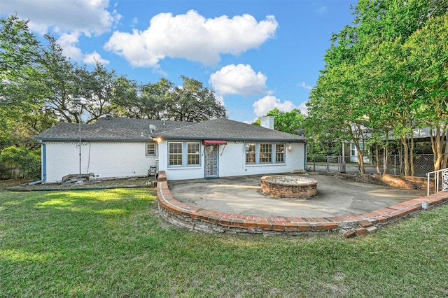 back of property with a fire pit, a patio area, and a lawn