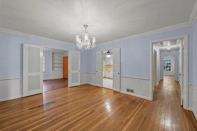 unfurnished dining area with wood-type flooring, built in shelves, ornamental molding, and a notable chandelier