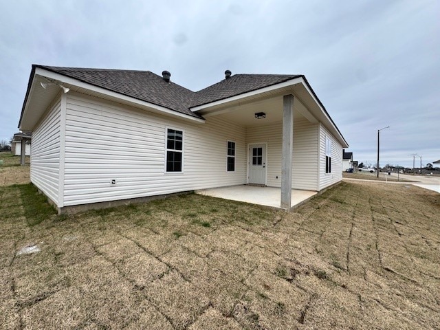 rear view of property with a yard, roof with shingles, and a patio area