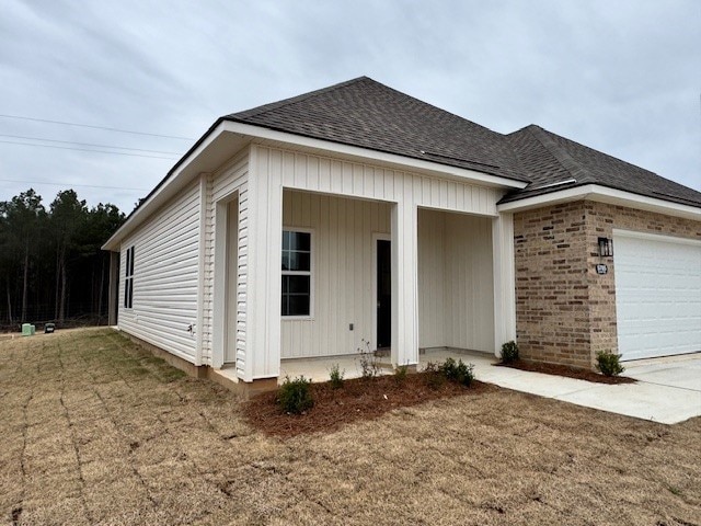 view of front of home with a garage, a front yard, roof with shingles, and brick siding