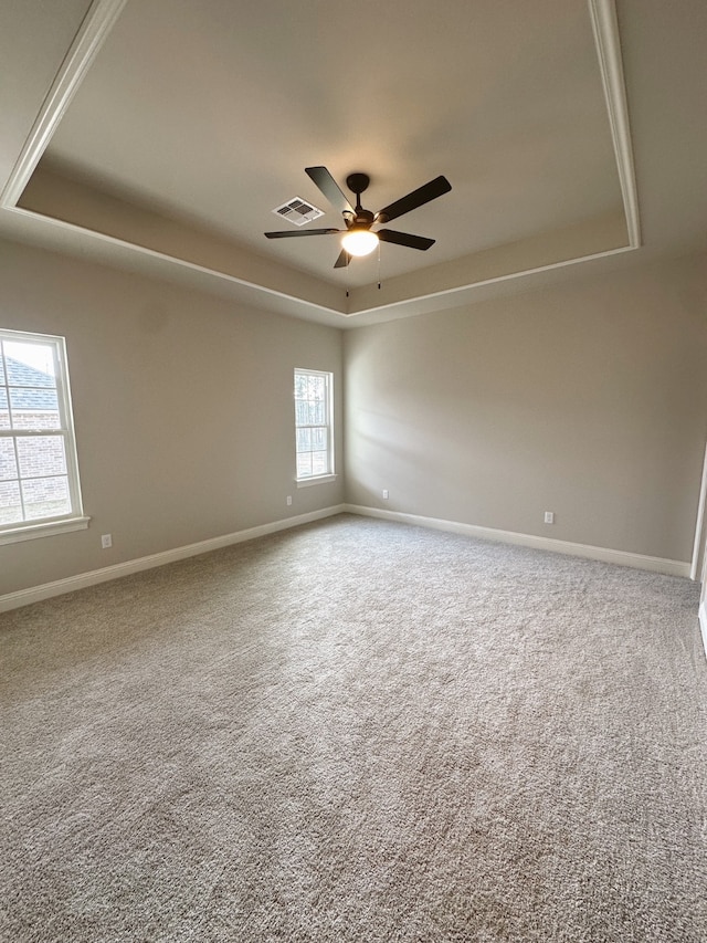 carpeted spare room featuring a ceiling fan, a tray ceiling, visible vents, and baseboards