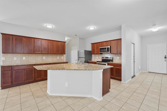 kitchen with a center island with sink, light stone counters, stainless steel appliances, and backsplash