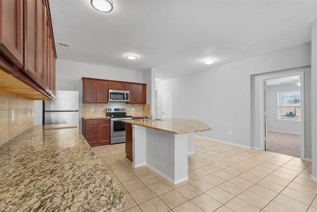 kitchen featuring tasteful backsplash, light stone countertops, an island with sink, appliances with stainless steel finishes, and light tile patterned floors