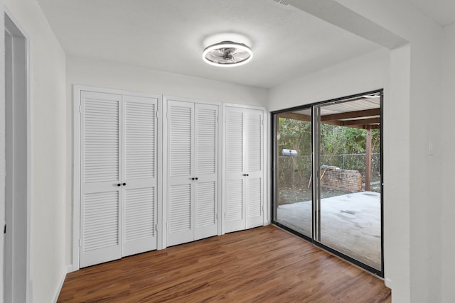 unfurnished bedroom featuring hardwood / wood-style floors, access to exterior, and two closets