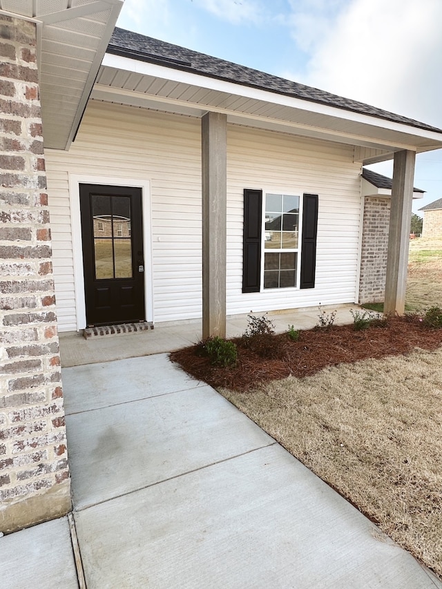 view of exterior entry featuring covered porch, brick siding, and roof with shingles