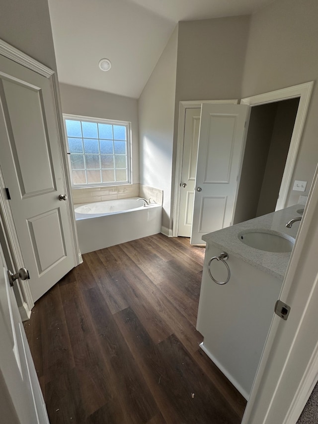 bathroom with a washtub, hardwood / wood-style floors, vanity, and vaulted ceiling