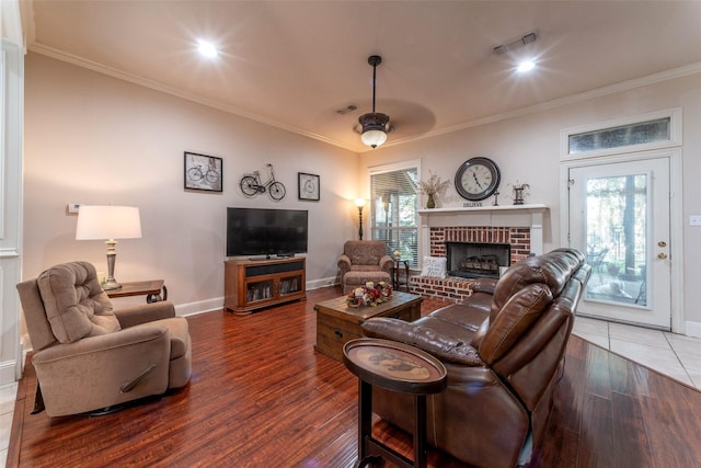 living room featuring ceiling fan, dark hardwood / wood-style floors, ornamental molding, and a brick fireplace