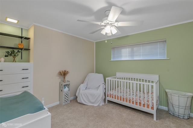 carpeted bedroom featuring ornamental molding, a crib, and ceiling fan