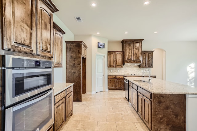 kitchen featuring tasteful backsplash, sink, light stone counters, an island with sink, and appliances with stainless steel finishes