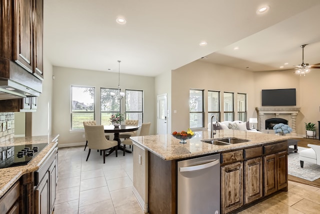 kitchen with a center island with sink, sink, light stone countertops, hanging light fixtures, and black electric stovetop