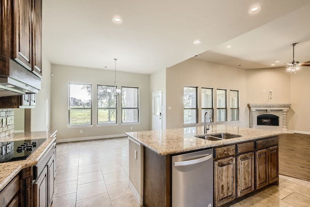 kitchen featuring light stone counters, sink, decorative light fixtures, a center island with sink, and black electric stovetop