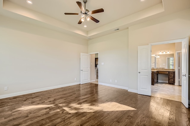 empty room featuring ceiling fan, a tray ceiling, hardwood / wood-style floors, and a high ceiling