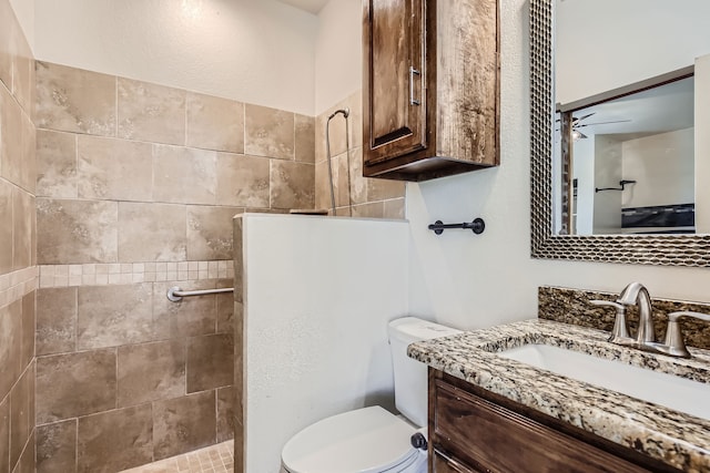 bathroom featuring ceiling fan, tiled shower, vanity, and toilet