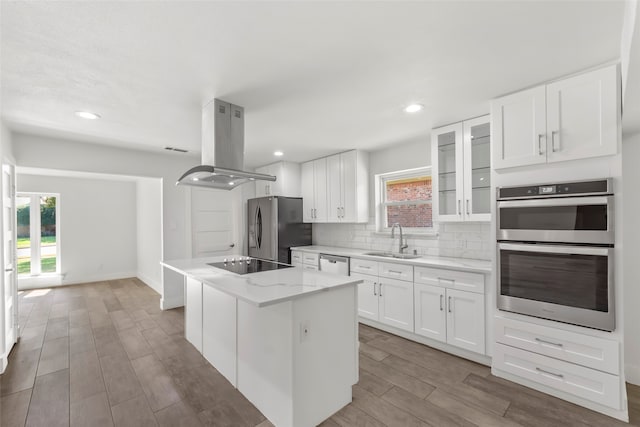 kitchen with island range hood, sink, white cabinets, and appliances with stainless steel finishes