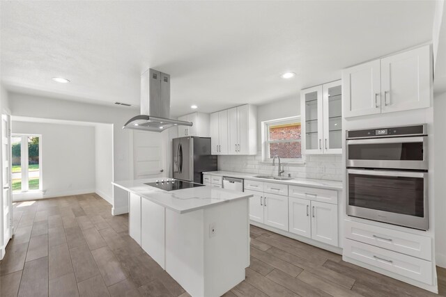 kitchen featuring light stone countertops, island exhaust hood, white cabinetry, and stainless steel appliances