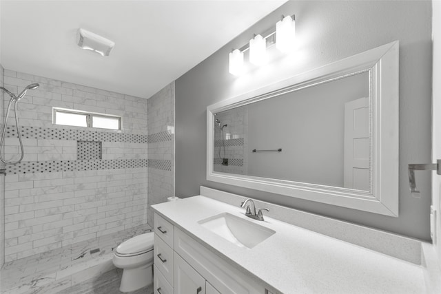 bathroom with a tile shower, vanity, and toilet