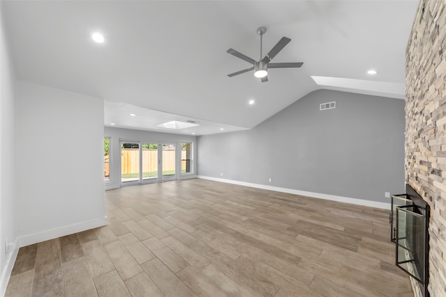 unfurnished living room featuring light wood-type flooring, lofted ceiling with skylight, ceiling fan, and a stone fireplace