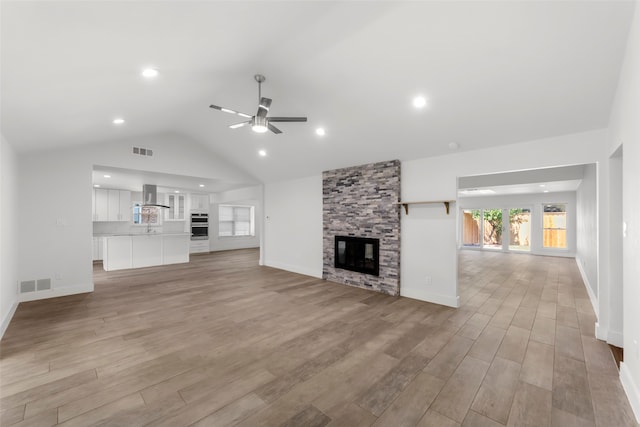 unfurnished living room with ceiling fan, a stone fireplace, lofted ceiling, and light hardwood / wood-style flooring