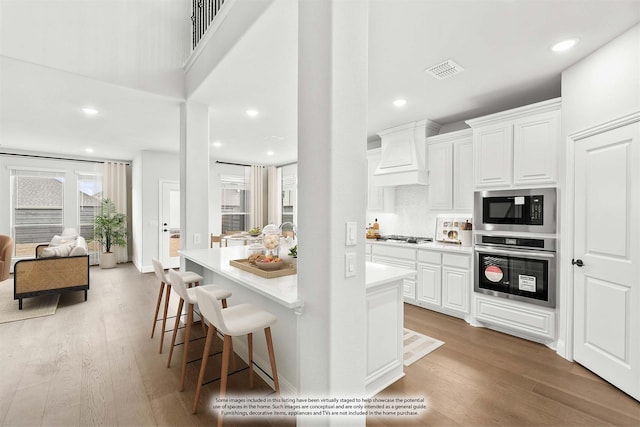 kitchen with white cabinets, stainless steel appliances, custom range hood, and light hardwood / wood-style flooring