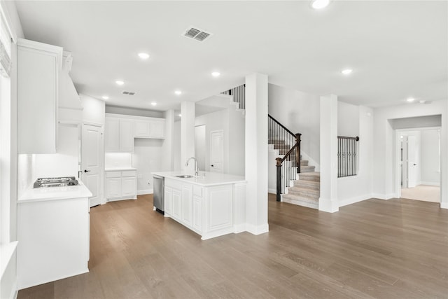 kitchen featuring appliances with stainless steel finishes, light wood-type flooring, white cabinets, sink, and a kitchen island with sink