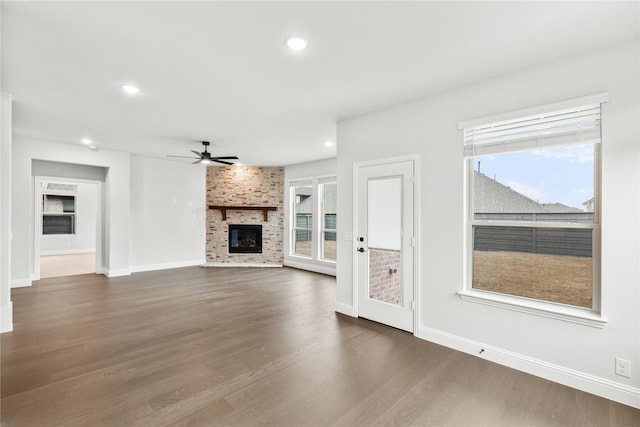 unfurnished living room with a large fireplace, ceiling fan, dark hardwood / wood-style flooring, and plenty of natural light