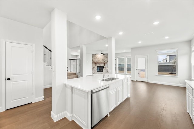 kitchen featuring white cabinetry, light hardwood / wood-style floors, sink, a large fireplace, and dishwasher