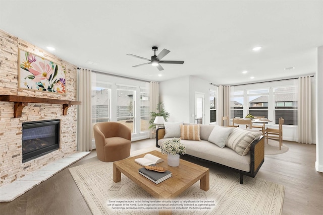 living room with ceiling fan, light hardwood / wood-style floors, and a stone fireplace