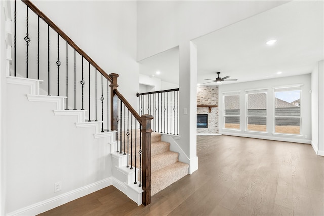 stairway featuring a fireplace, hardwood / wood-style floors, and ceiling fan