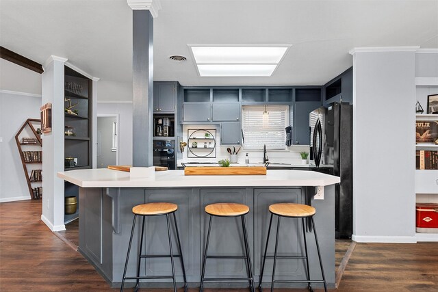 kitchen with black appliances, a breakfast bar area, light countertops, and dark wood-style floors