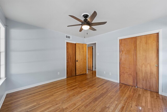 unfurnished bedroom with wood finished floors, a closet, baseboards, visible vents, and a ceiling fan