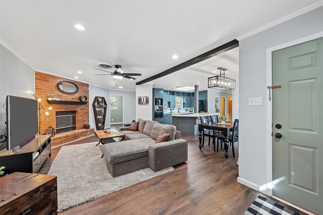 living room featuring ceiling fan, dark wood-style flooring, recessed lighting, ornamental molding, and a brick fireplace
