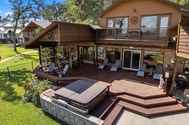 rear view of property with a wooden deck, a balcony, a lawn, and a covered hot tub