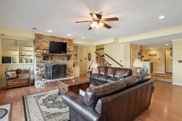 living room featuring crown molding, ceiling fan, wood-type flooring, a brick fireplace, and built in shelves