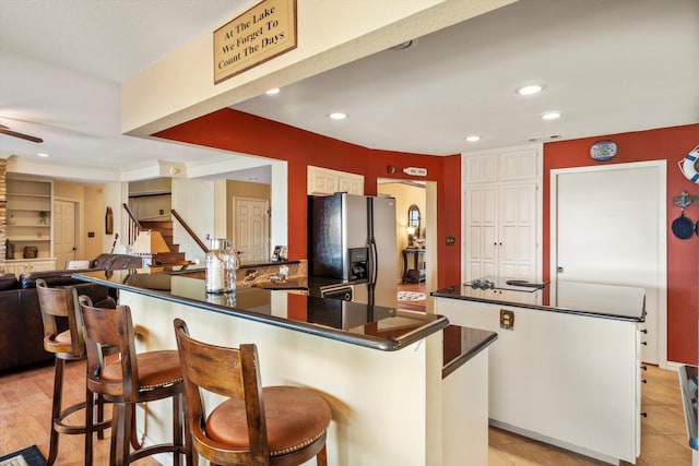 kitchen featuring white cabinets, a kitchen bar, a center island, ceiling fan, and stainless steel refrigerator with ice dispenser