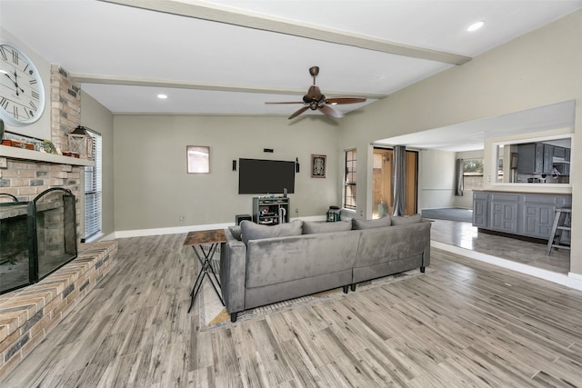 living room with beamed ceiling, a brick fireplace, light hardwood / wood-style flooring, and ceiling fan