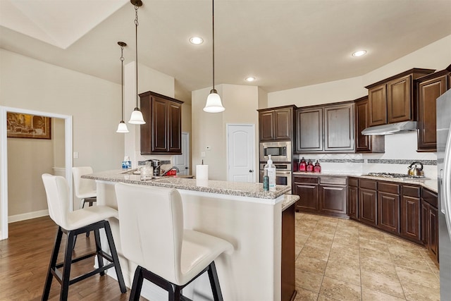 kitchen featuring a kitchen breakfast bar, appliances with stainless steel finishes, dark brown cabinets, and pendant lighting