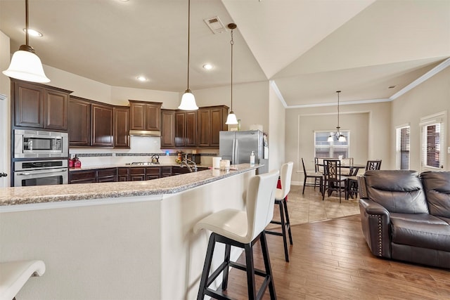 kitchen featuring stainless steel appliances, wood-type flooring, vaulted ceiling, and hanging light fixtures