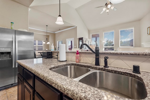 kitchen with lofted ceiling, hanging light fixtures, sink, stainless steel fridge, and light stone counters