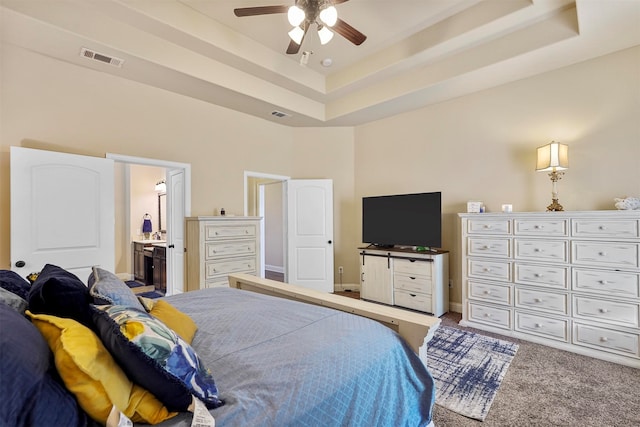 carpeted bedroom featuring ceiling fan, a raised ceiling, ensuite bathroom, and a high ceiling