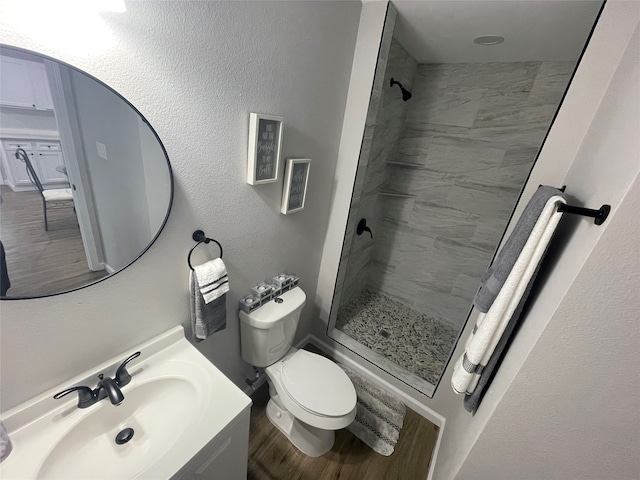 bathroom with a tile shower, hardwood / wood-style flooring, vanity, and toilet