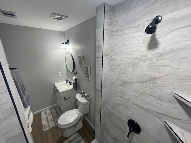 bathroom with wood-type flooring, vanity, toilet, and tiled shower