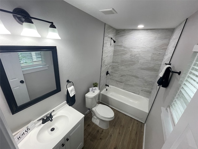 full bathroom featuring vanity, hardwood / wood-style floors, tiled shower / bath, and toilet