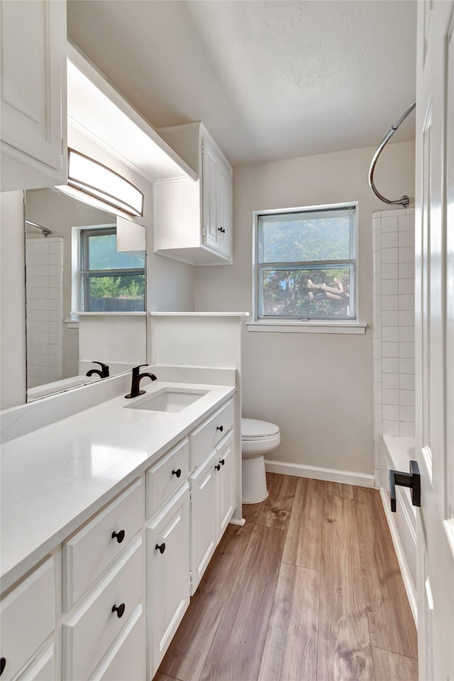 full bathroom with wood-type flooring, tiled shower / bath combo, vanity, and toilet