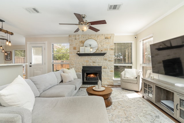 living room featuring light wood-type flooring, ceiling fan, a fireplace, and crown molding