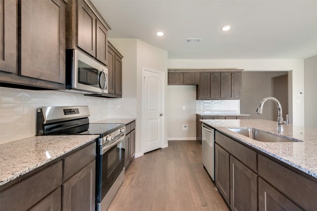 kitchen featuring light stone countertops, sink, light wood-type flooring, and stainless steel appliances