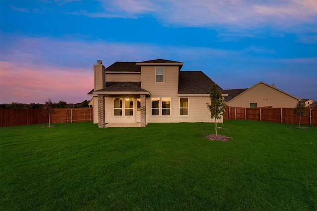 back house at dusk featuring a lawn and a patio