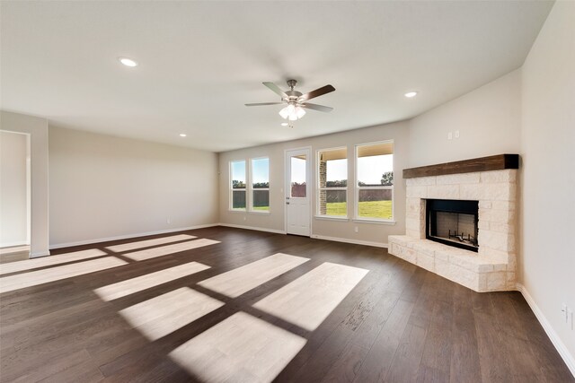 unfurnished living room featuring a stone fireplace, ceiling fan, and dark wood-type flooring