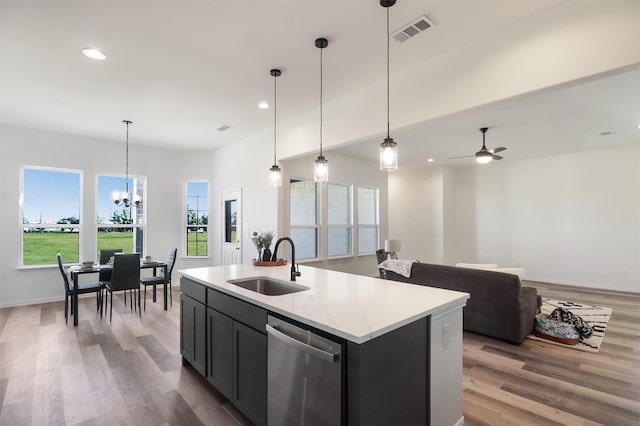 kitchen featuring stainless steel dishwasher, sink, decorative light fixtures, and an island with sink