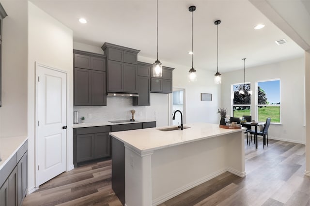 kitchen featuring pendant lighting, sink, backsplash, light stone countertops, and an island with sink