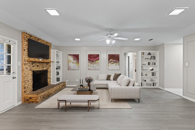 living room featuring built in shelves, a brick fireplace, hardwood / wood-style floors, and ceiling fan